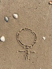 In the sand on the beach is carved the sign for female