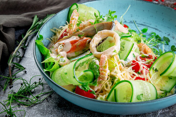 Green salad with seafood. Fresh salad of sliced cucumbers, oyster, squid rings, shrimp, cherry tomatoes, spinach and grated cheese