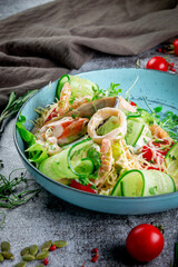 Green salad with seafood. Fresh salad of sliced cucumbers, oyster, squid rings, shrimp, cherry tomatoes, spinach and grated cheese