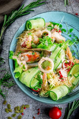 Green salad with seafood. Fresh salad of sliced cucumbers, oyster, squid rings, shrimp, cherry tomatoes, spinach and grated cheese