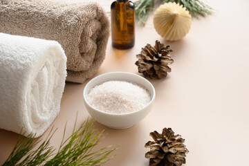 Obraz na płótnie Canvas Winter body care and composition with sea salt, aroma oil, pine cones, towel, evergreen branches for relax in bath or sauna on beige background. Close up.