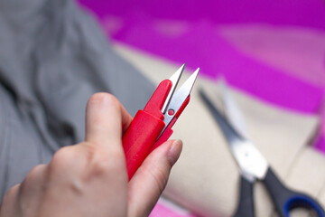 Scissors in hand against the background of different fabrics and tailor's accessories