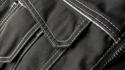 White stitching on black fabric. Texture black working clothes with white stitching closeup, green...
