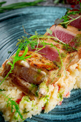 Fried tuna fillet with couscous and herbs on a gray stone table.