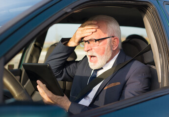 Senior businessman using tablet for traffic navigation while sitting in the car on the parking lot