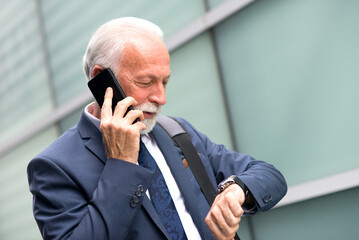 Senior businessman talking on the smart phone in front of corporate office building