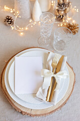 Fototapeta na wymiar Festive christmas table setting with golden cutlery and porcelain plate and christmas decoration. Mockup for place card, dinner invitation, restaurant menu template. Copy space