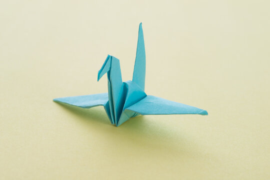 Blue origami paper crane on yellow background
