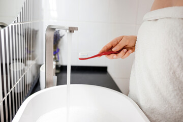 Close up of woman hand holding toothbrush with toothpaste while standing in bathroom