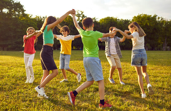 Group of kids playing games and having fun in nature. Joyful little children dancing a round dance on green grass in the park. Several happy little friends holding hands and running in a circle