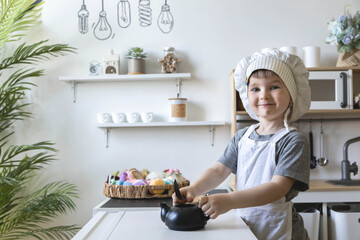 Cute little baby boy in chef hat and apron playing at childish kitchen cooking food back view