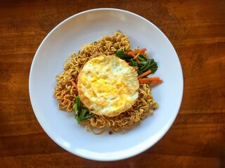 noodles with shrimp, fried noodles with green vegetables with omelette on white plate with fork on wooden table close up