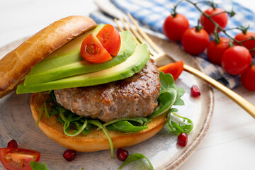 Toasted bagel with premium beef burger, arugula, and avocado slices.