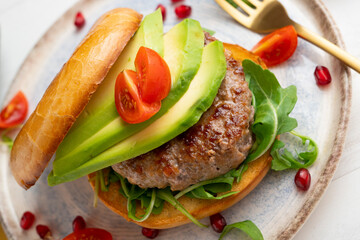 Toasted bagel with premium beef burger, arugula, and avocado slices.