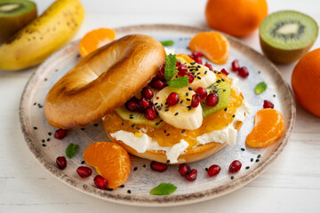 Toasted bagel with orange marmalade, cream cheese, tangerine, kiwi, banana and pomegranate. vegan breakfast. Superfood vegan brunch.