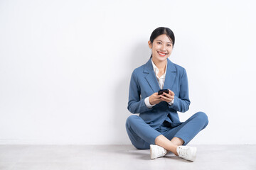 Image of young Asian businesswoman sitting on floor and using smartphone