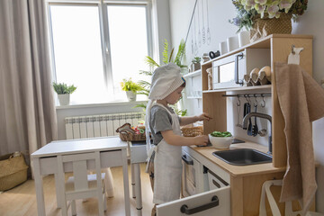 Cute little baby boy in chef hat and apron playing at childish kitchen cooking food back view