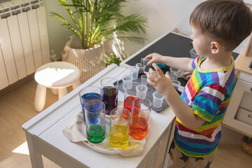 Cute baby boy learning mixing different colors with water and paint in containers. Early development