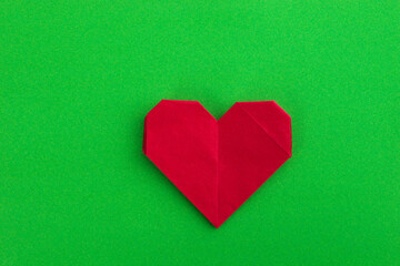 Red origami heart on green background
