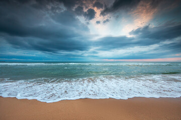 Fototapeta na wymiar Dramatic cloudscape over the sea waves and beach