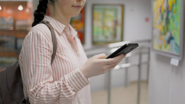 Culture and education. Close up of woman using a smartphone. Virtual excursion with audio guide in the art gallery. Slow motion. Exhibition and visit to the museum.