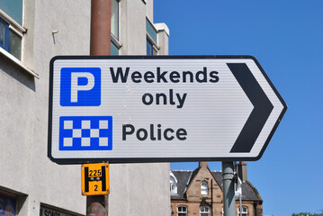 Close Up of Road Sign and Symbols 'Weekends Only' and 'Police' against Blue Sky and Building 