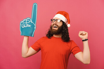 Victorious man wearing Christmas cap and fan glove over pink background.