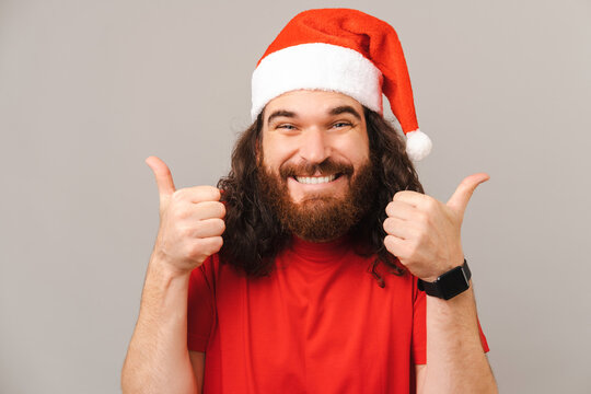 Handsome bearded man is showing two thumbs up while wearing Christmas cap.
