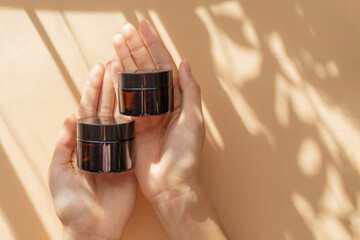 Two jars of moisturizer in women's hands. Amber glass bottles with gel, shampoo, cosmetic, close-up...