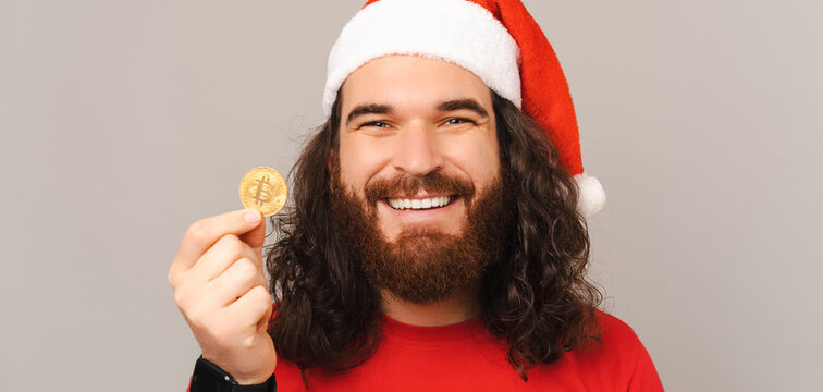 Banner photo of a young bearded man wearing Christmas hat is holding a bitcoin.
