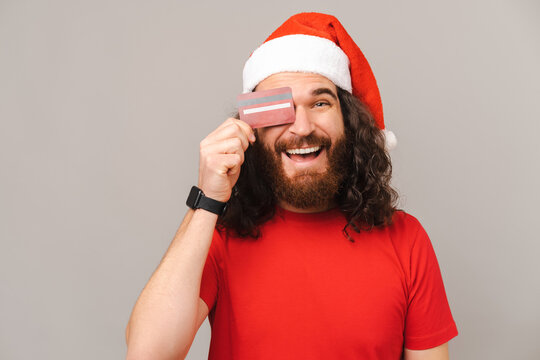 Smiling bearded man wearing Christmas cap covers one eye with a red card.