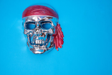 a silver skull with a red headband on a blue background. Halloween, piracy. Jolly Roger. The sign...