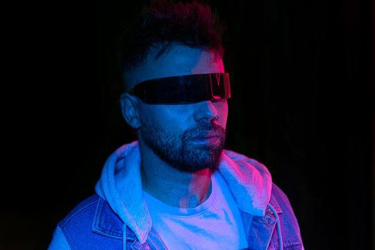 Neon light studio close-up portrait of serious man model with mustaches and beard in cyberpunk sunglasses 