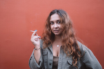 Woman smoking a cigarette standing by coral background.
