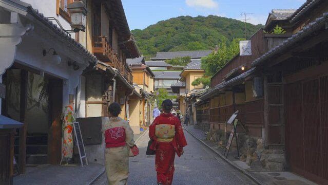 Shot of a traditional street of Kyoto during a sunny day with two girls dressed in kimono walking away