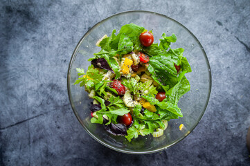 Glass bowl with fresh salad, greens, avocado and vegetables. Healthy food concept. Rustic style, top view