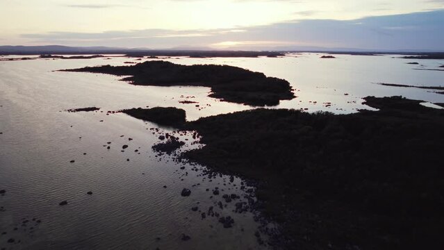 Beautiful aerial flying over gigantic irish lough (lake) corrib with many small island silhouettes in the water beneath. view into the distance. Flying forward, blue hour golden evening sun reflecting