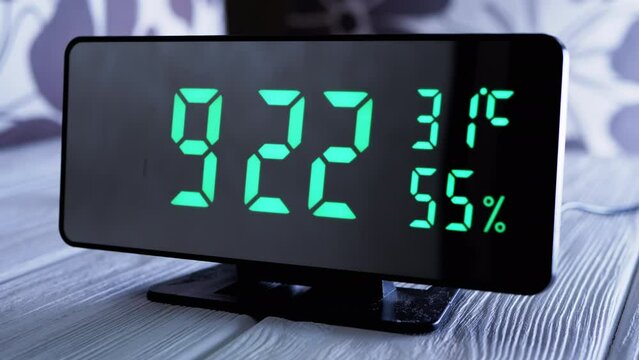 Digital Clock Showing Time on Green Display 9:22 AM, Temperature, Air Humidity. Modern mirror clock, alarm clock with a thermometer, hydrometer standing on a desk on white background. Time concept.