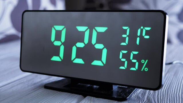 Digital Clock Showing Time on Green Display 9:25 AM, Temperature, Air Humidity. Modern mirror clock, alarm clock with a thermometer, hydrometer standing on a desk on white background. Time concept.