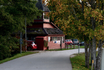 a dark red log building on the edge of a nature park with yellow-green trees and an asphalt pedestrian path