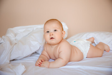 baby boy in a diaper is lying on a white sheet, covered with a blanket in the bedroom on the bed