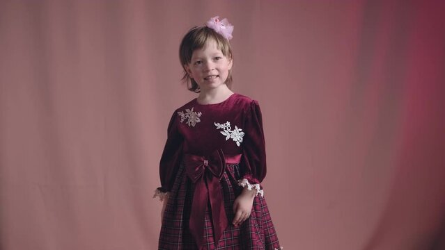 Cute little girl in an vintage burgundy dress is spinning in the dance and rejoicing. The concept of children theater productions and developing acting circles. Pink background