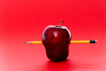 Yellow pencil through an apple on red background