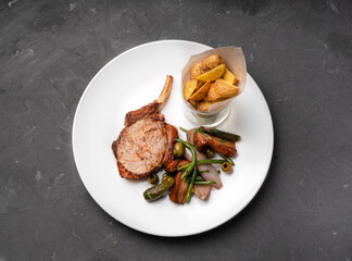 Meat on the bone loin on a white plate with a side dish of potatoes