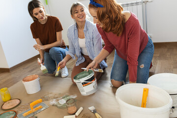Female roommates preparing and mixing paint to decorate walls in their home.	
