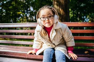 Beautiful little girl in eyeglasses with down syndrome smiling and looking into camera with cute...