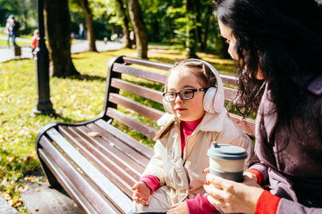 Special need child wearing headphones and happy time to use a smartphone on bench with her mother...