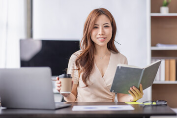 Asian Businesswoman holding notes and working on a laptop computer in the workplace, doing document planning analyzing the financial report, business plan investment, finance analysis concept.