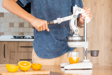 Teenager making fresh orange juice at the kitchen. Boy squeezing citrus juice with special kitchen...