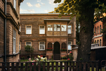 View of a two-story old wooden house in Liepaja with a carved balcony and a yard with a flower bed and a linden tree, traditional building
